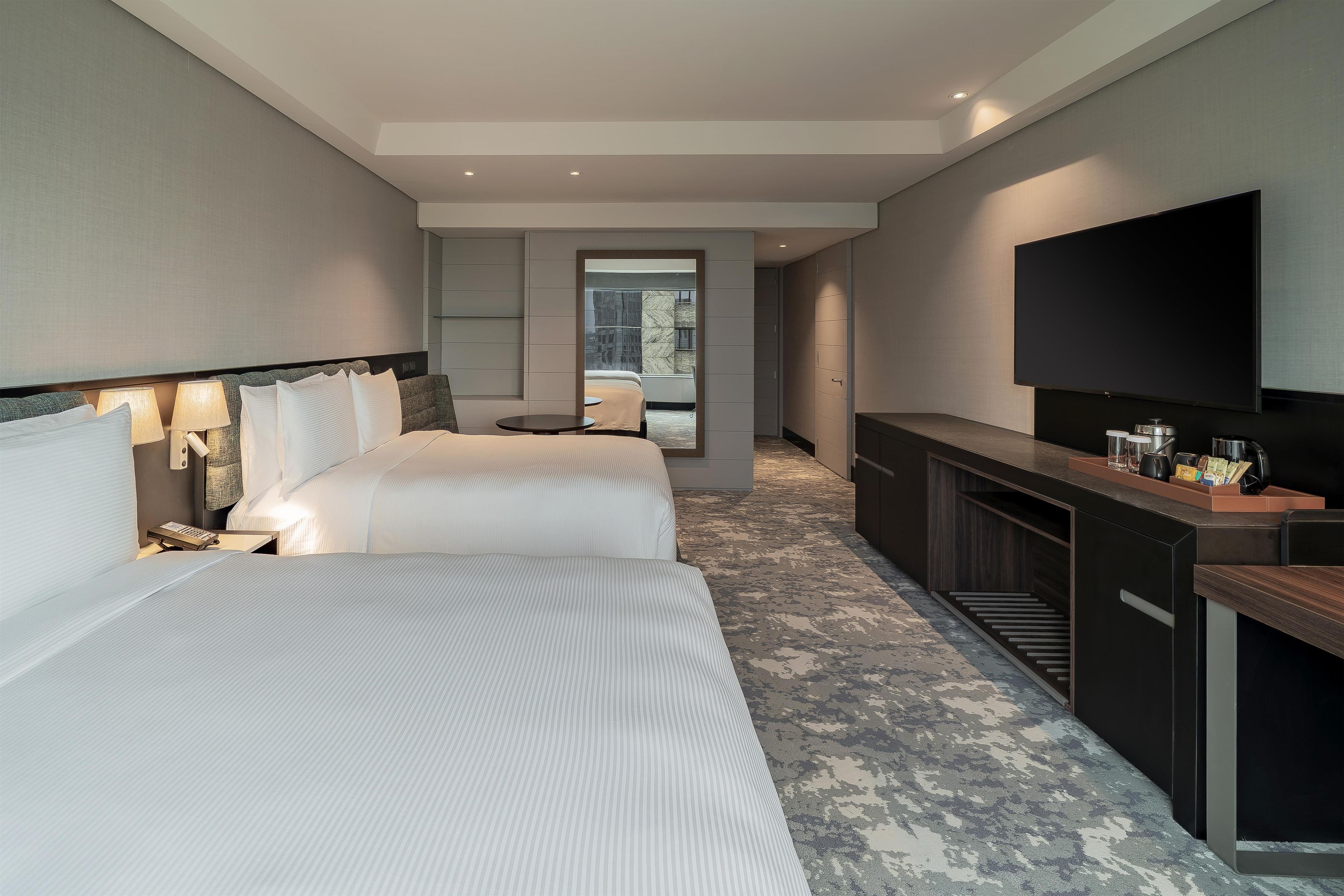 A hotel room with two beds, a TV, a minibar, and a view of the outdoors.