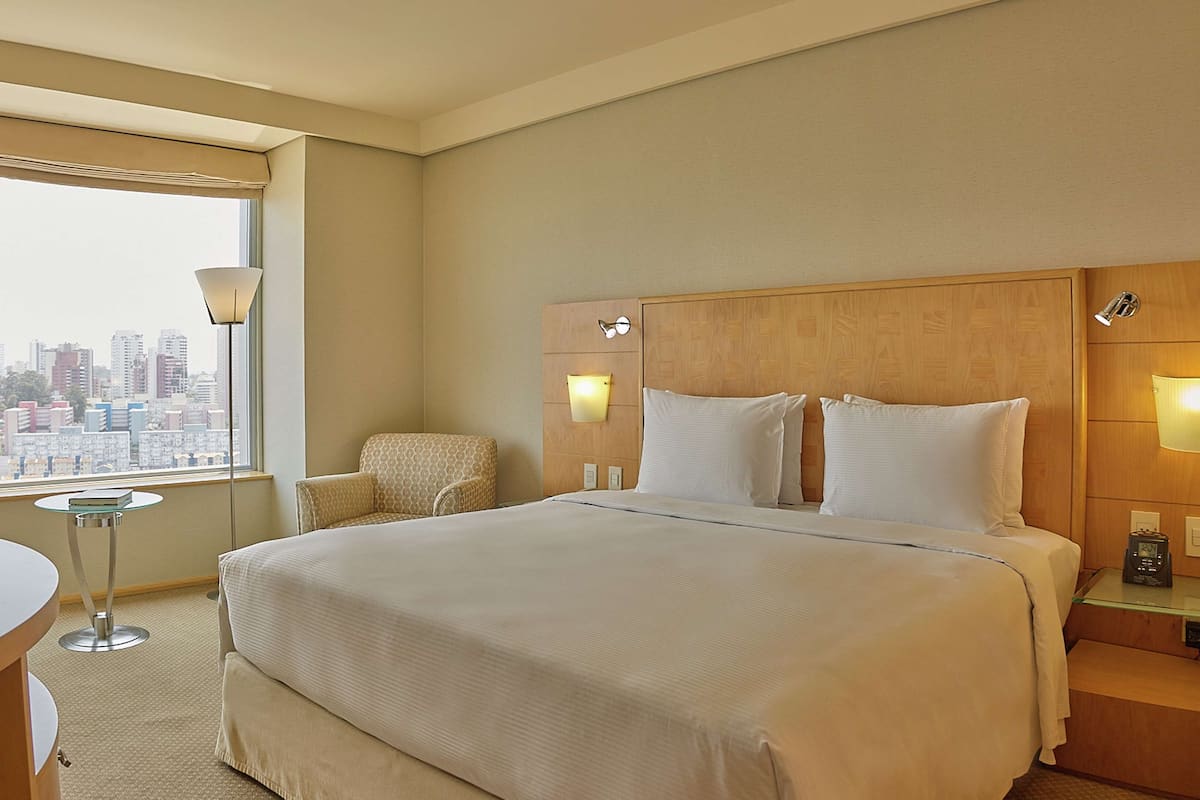 Habitación de hotel con una cama grande, una silla, un escritorio y vistas a la ciudad.