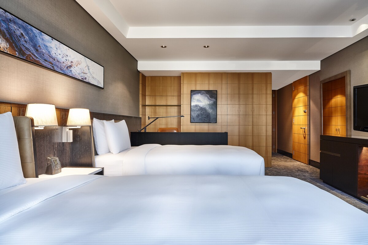 Hotelkamer met een groot bed, bedlampen, een bureau, een stoel, een televisie en een houten paneelwand.