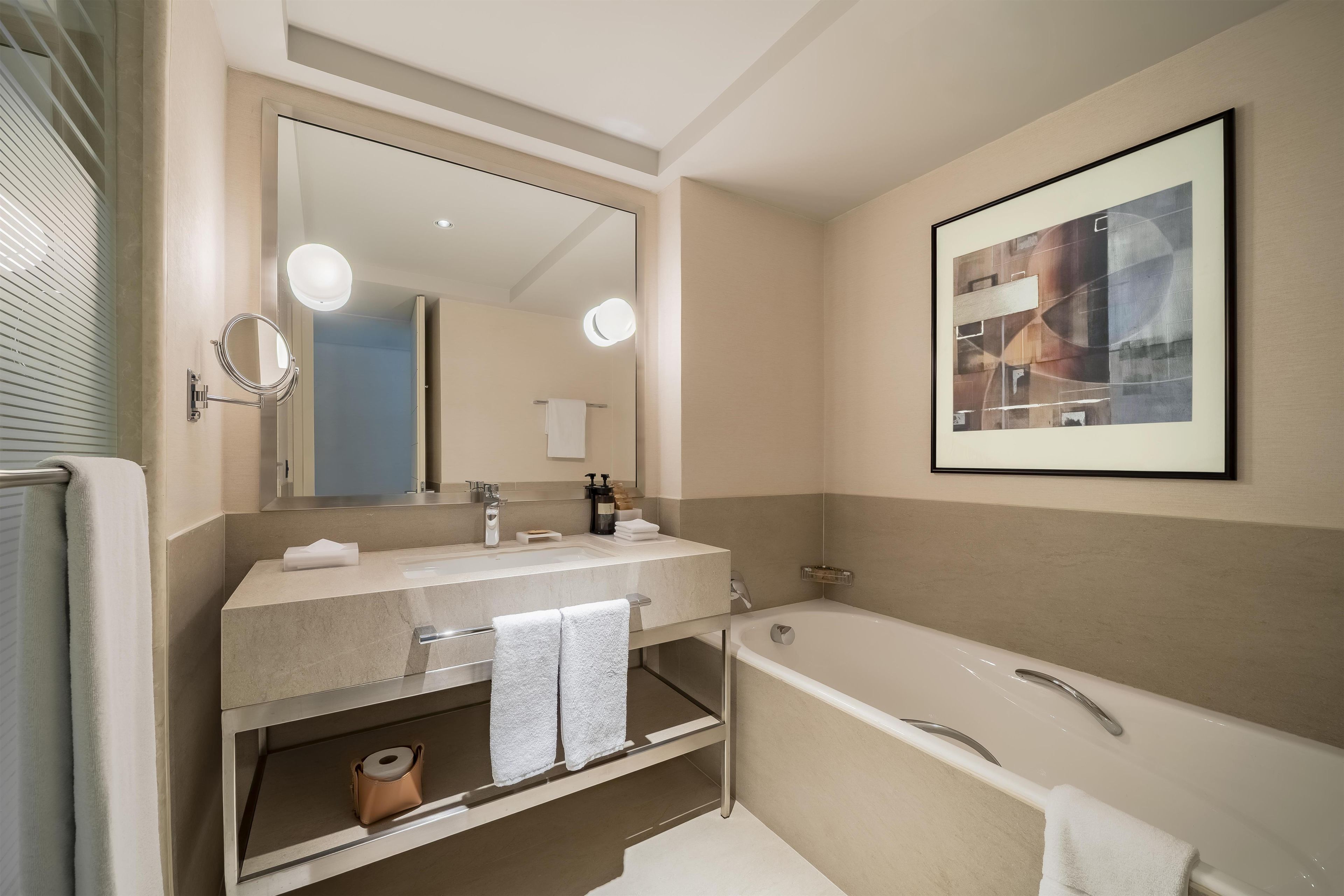 A modern bathroom with a large mirror, a bathtub, and a sink with a towel rack.