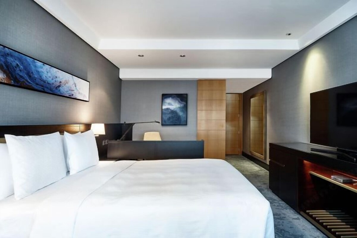 A modern hotel room with a large bed, a desk, a television, and artwork on the walls.