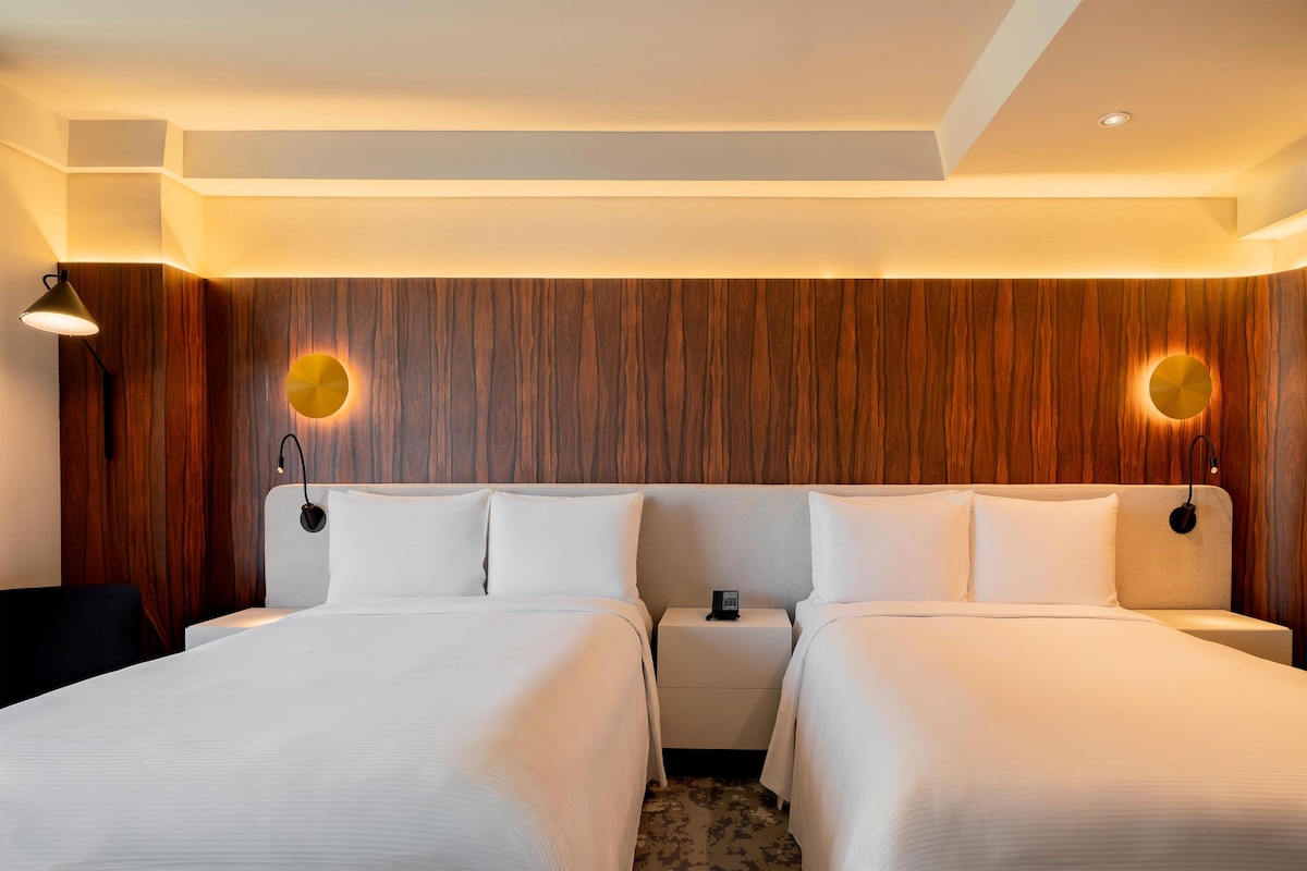 Een hotelkamer met twee bedden, een nachtkastje, een lamp en een wandlamp.