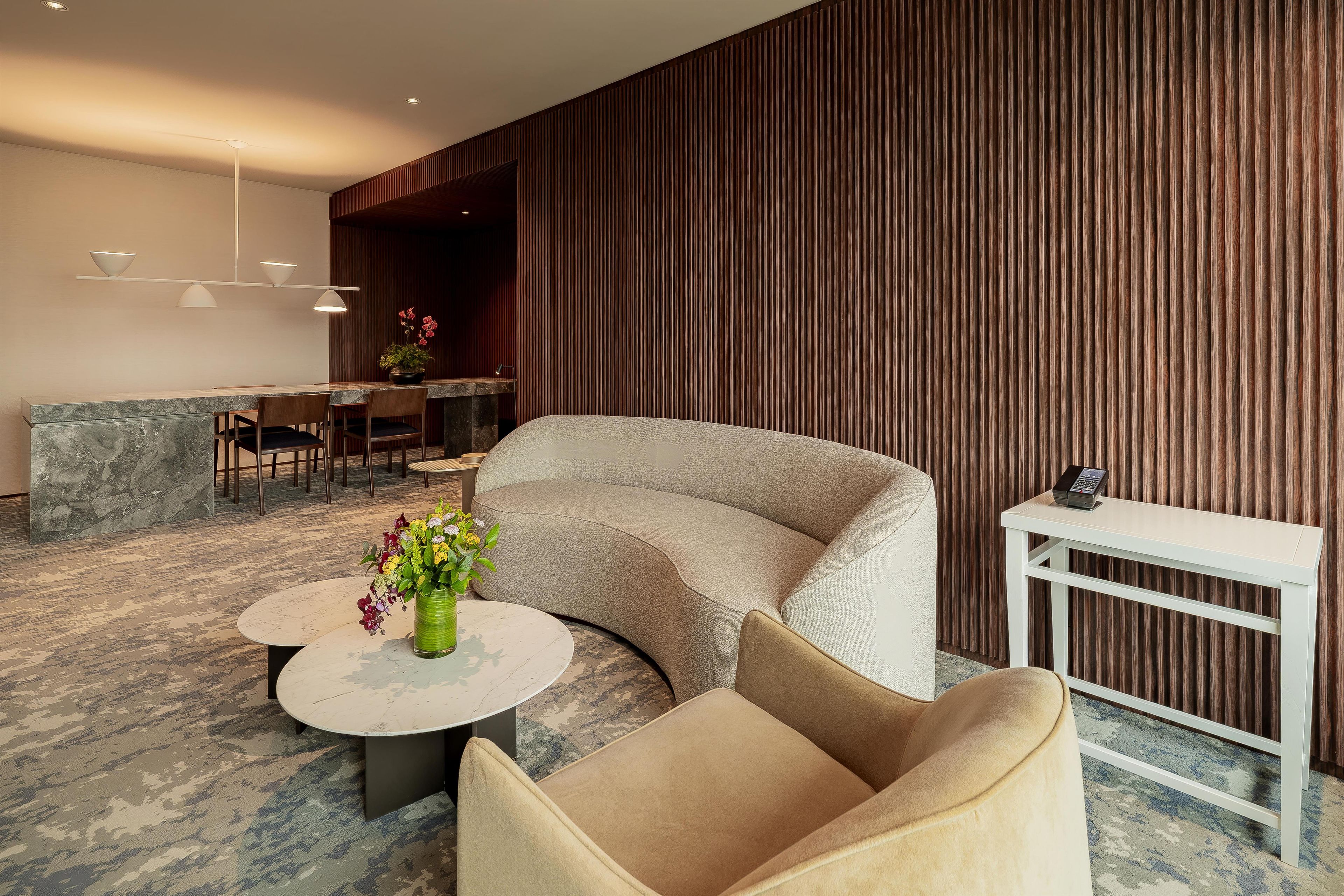 A modern lounge area with a curved sofa, a round table with a vase of flowers, and a small white table with a telephone.
