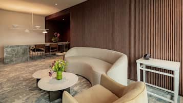 A modern lounge area with a curved sofa, a round table with a vase of flowers, and a small white table with a telephone.