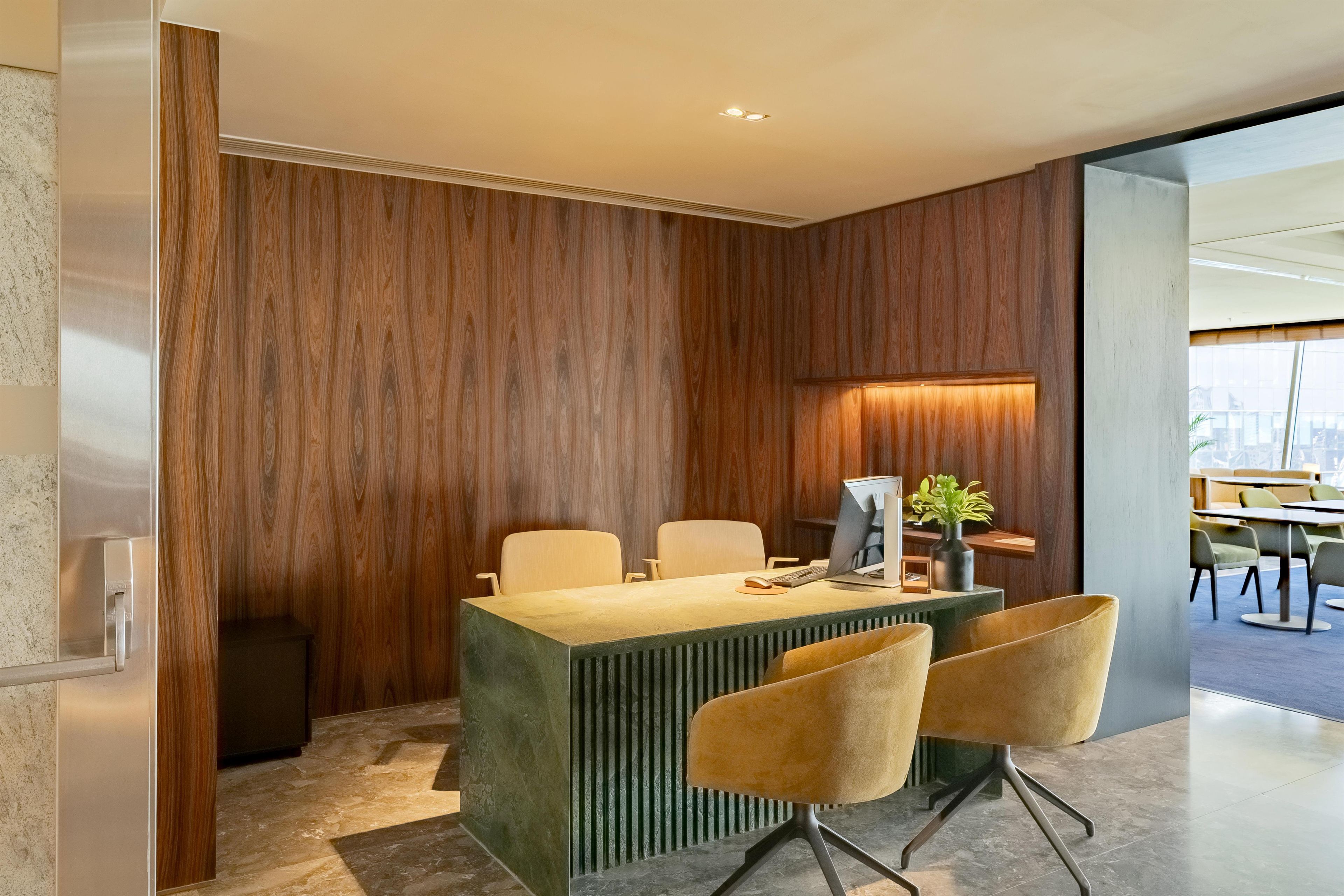 A modern office space with a wooden accent wall, a central desk with two chairs, and a computer setup.