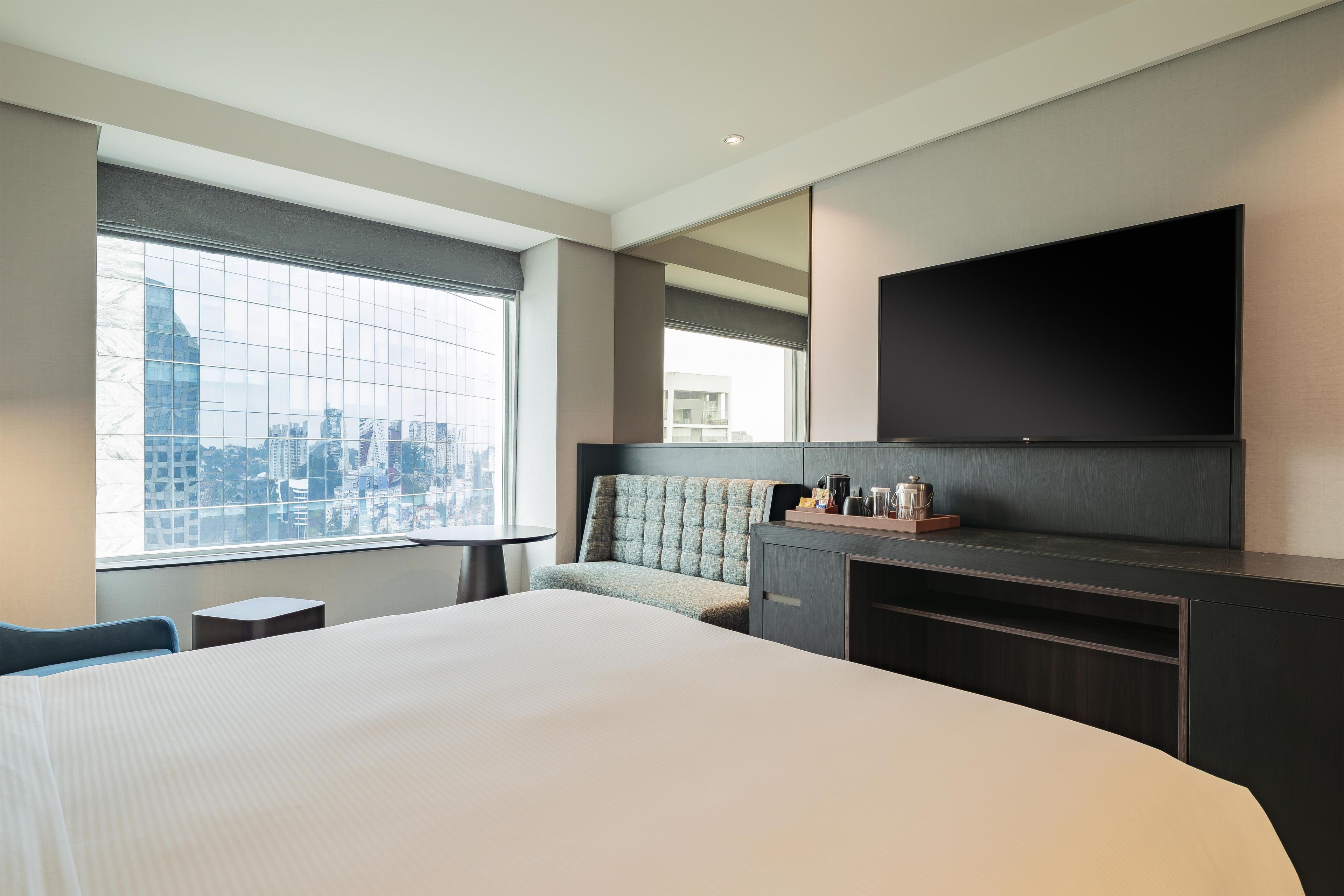 Een hotelkamer met een groot bed, een zithoek, een flatscreen televisie aan de muur en uitzicht op de stad.