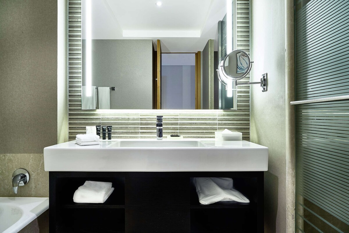 Een moderne badkamer met een grote spiegel, een witte wastafel en een handdoekrek.