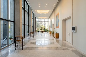Un hall d’hôtel spacieux, doté de grandes fenêtres, d’un espace salon central et d’un design moderne.