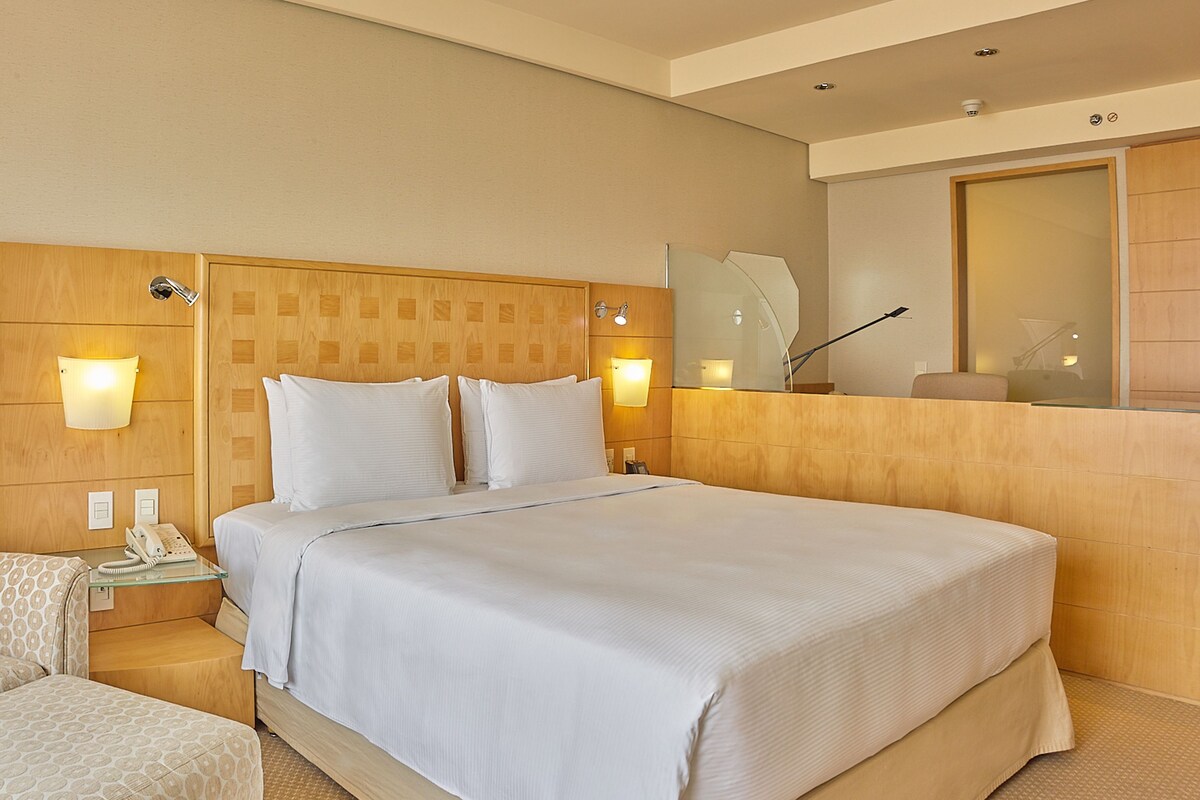 Een hotelkamer met een groot bed, bedlampen, een spiegel en een klein tafeltje met een telefoon.