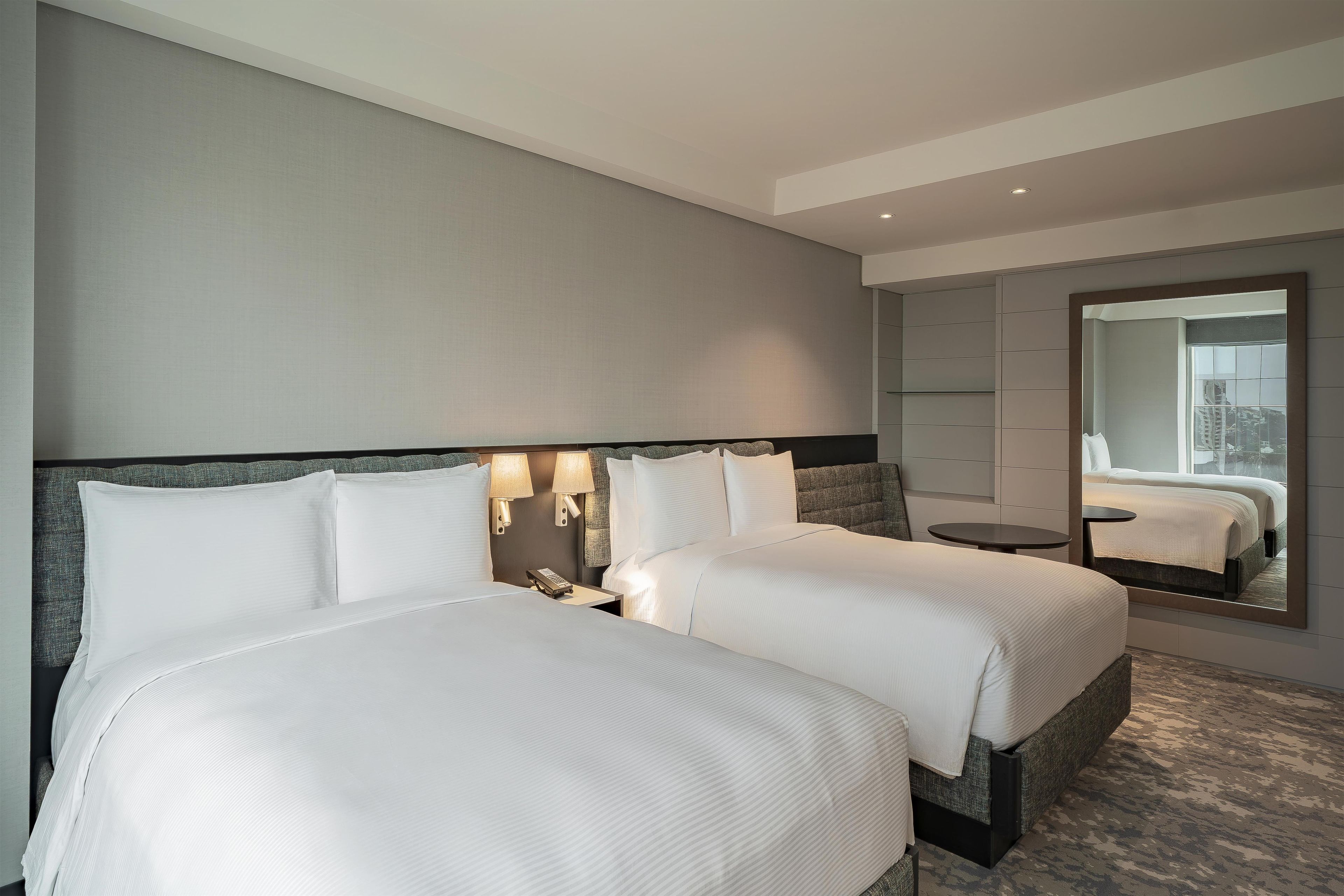 A hotel room with two beds, a large mirror, and a small round table.