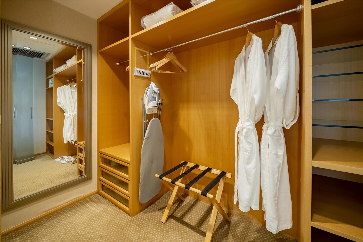 A hotel room with a wooden wardrobe, a mirror, and a bench.