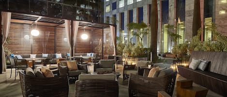 An outdoor seating area with wicker furniture, a stone wall, and a view of a modern building.