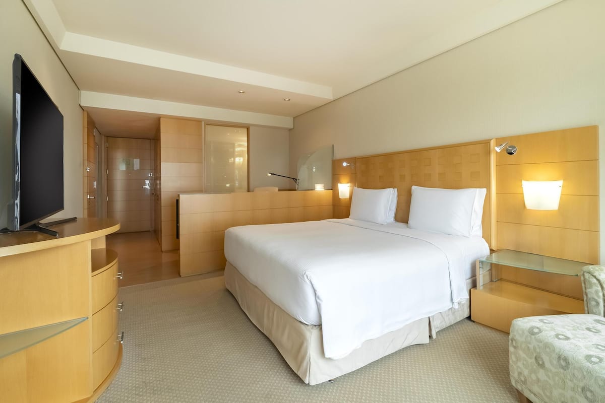 Habitación de hotel con una cama grande, televisión, escritorio y un separador de vidrio.