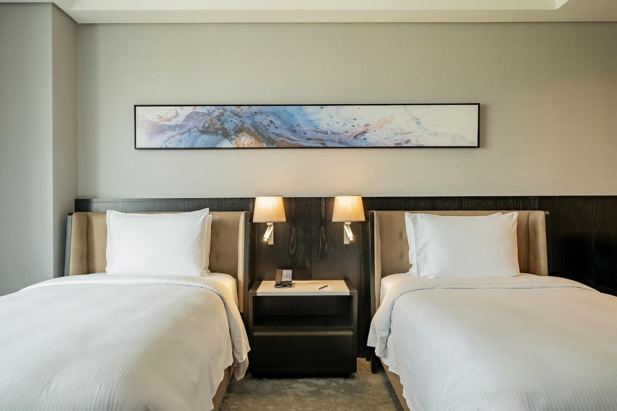 Habitación de hotel con dos camas, una mesita de noche, un cuadro en la pared y una lámpara.