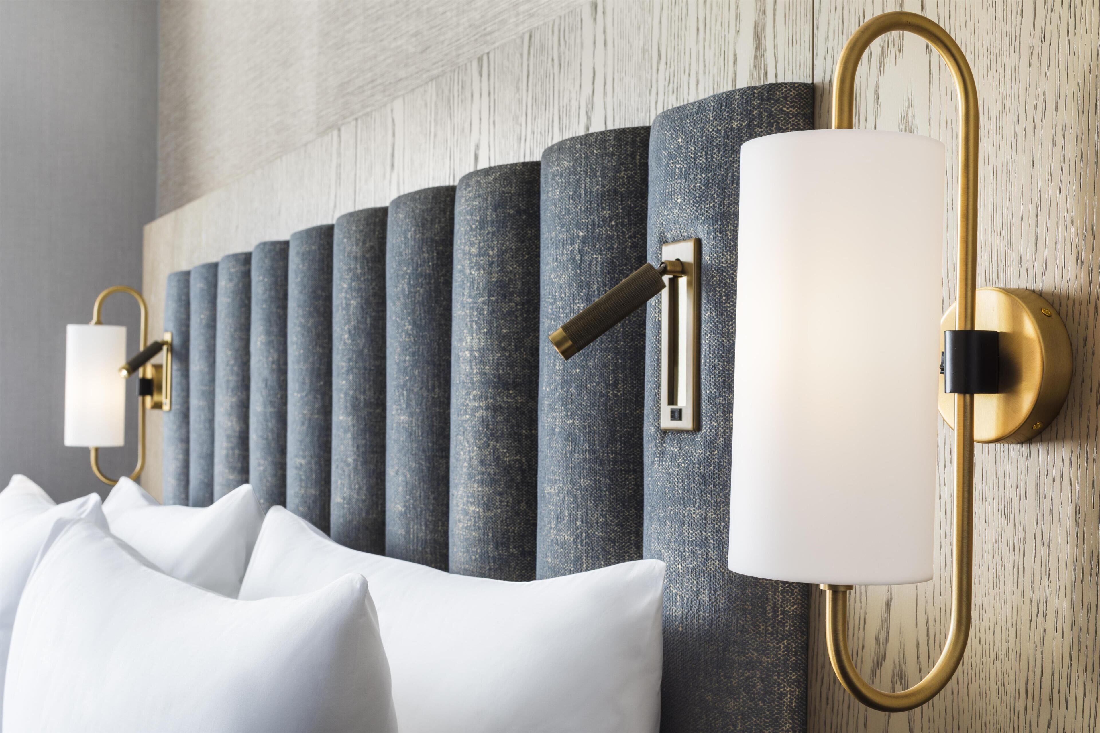 A modern hotel room with a headboard featuring a series of cylindrical columns and wall-mounted lamps.