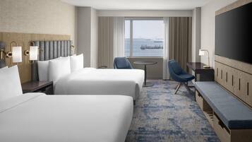 A hotel room with two beds, a desk, a chair, a TV, and a view of the water.