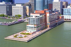 Un hotel moderno frente al río, con un llamativo letrero de 'Hyatt Regency', una amplia terraza al aire libre y vistas del río.