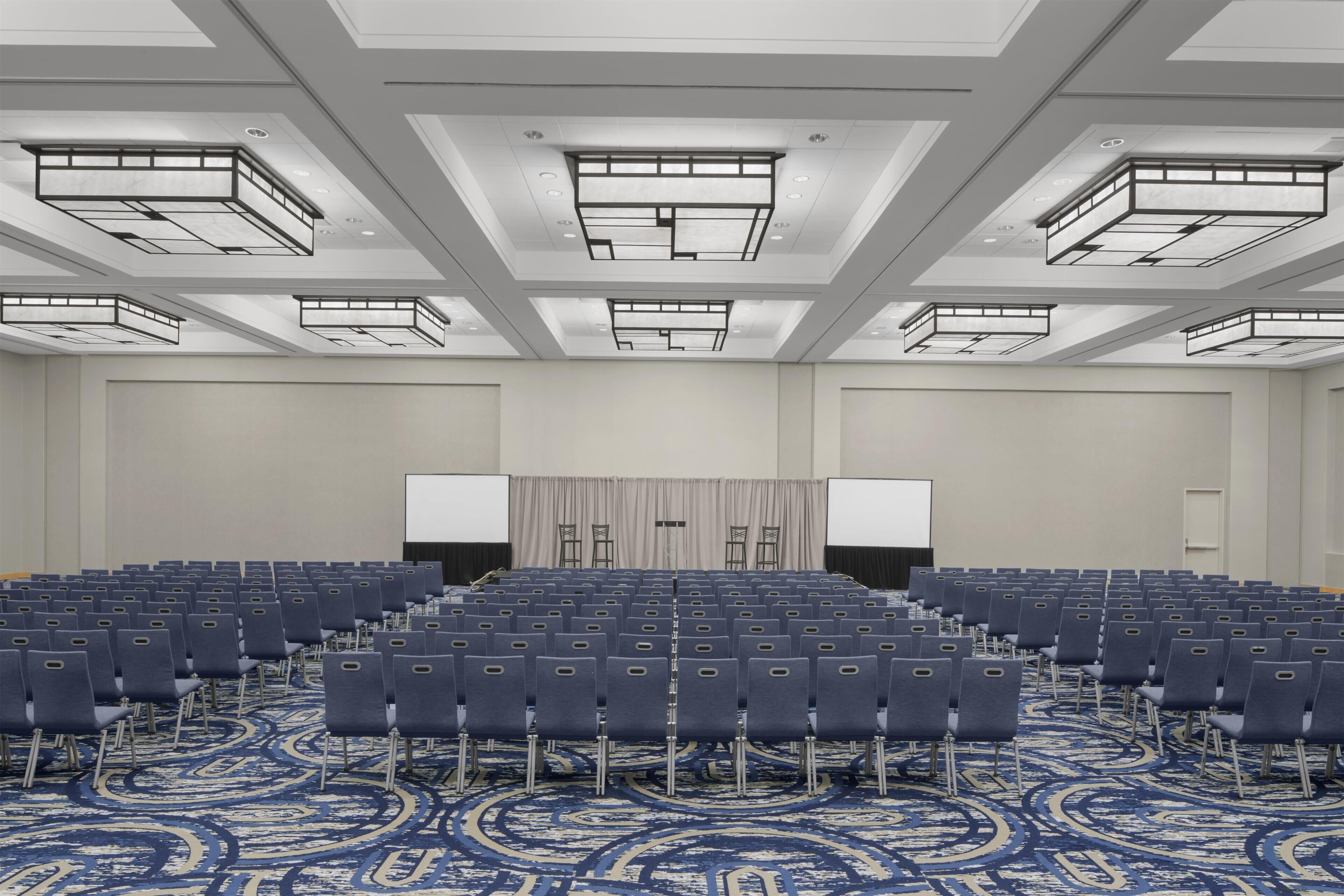 A conference room with rows of chairs, a stage with a screen, and a patterned carpet.