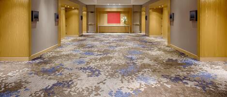 A hotel corridor with a patterned carpet, wooden doors, and a reception desk with a red accent wall.