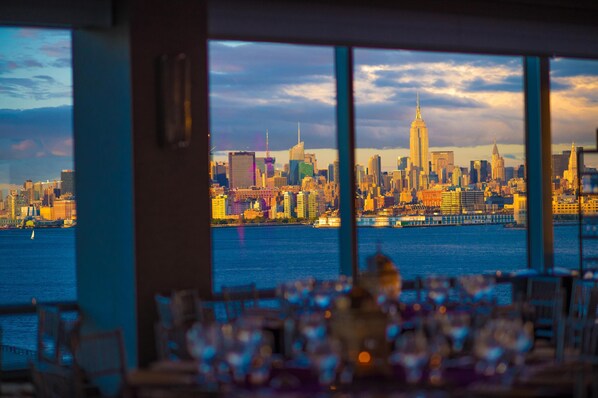 A view of a city skyline from a window overlooking a body of water, with a dining area in the foreground.
