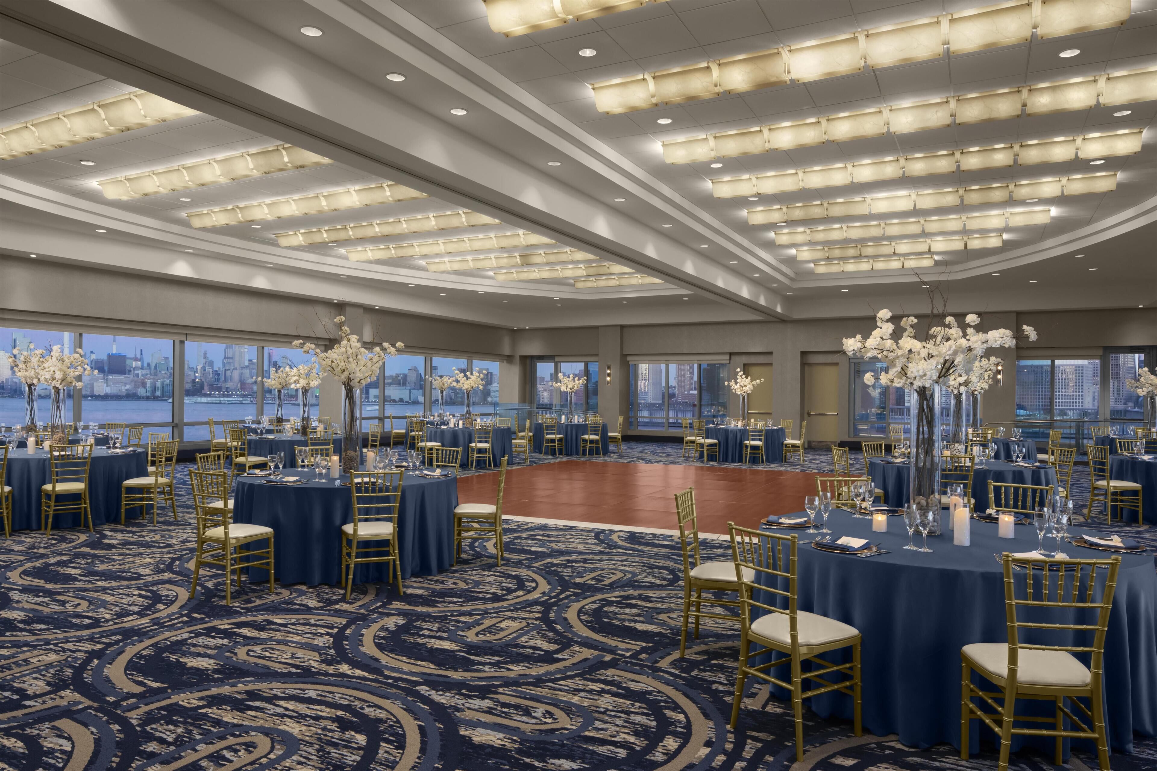A spacious banquet hall with round tables, gold chairs, and floral centerpieces.