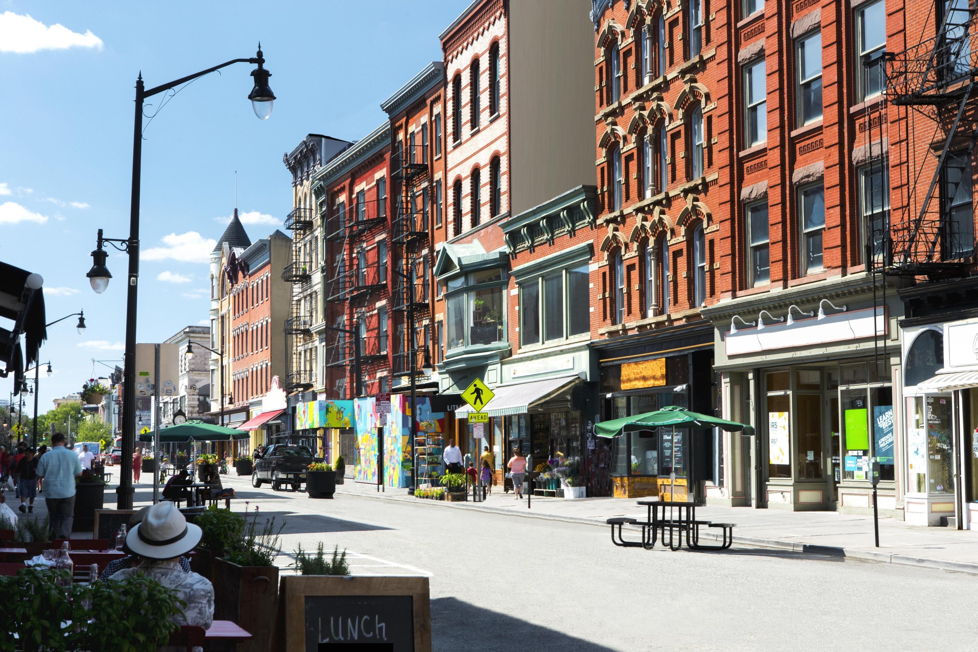 A street with red brick buildings, outdoor seating, and a sign indicating a lunch spot.