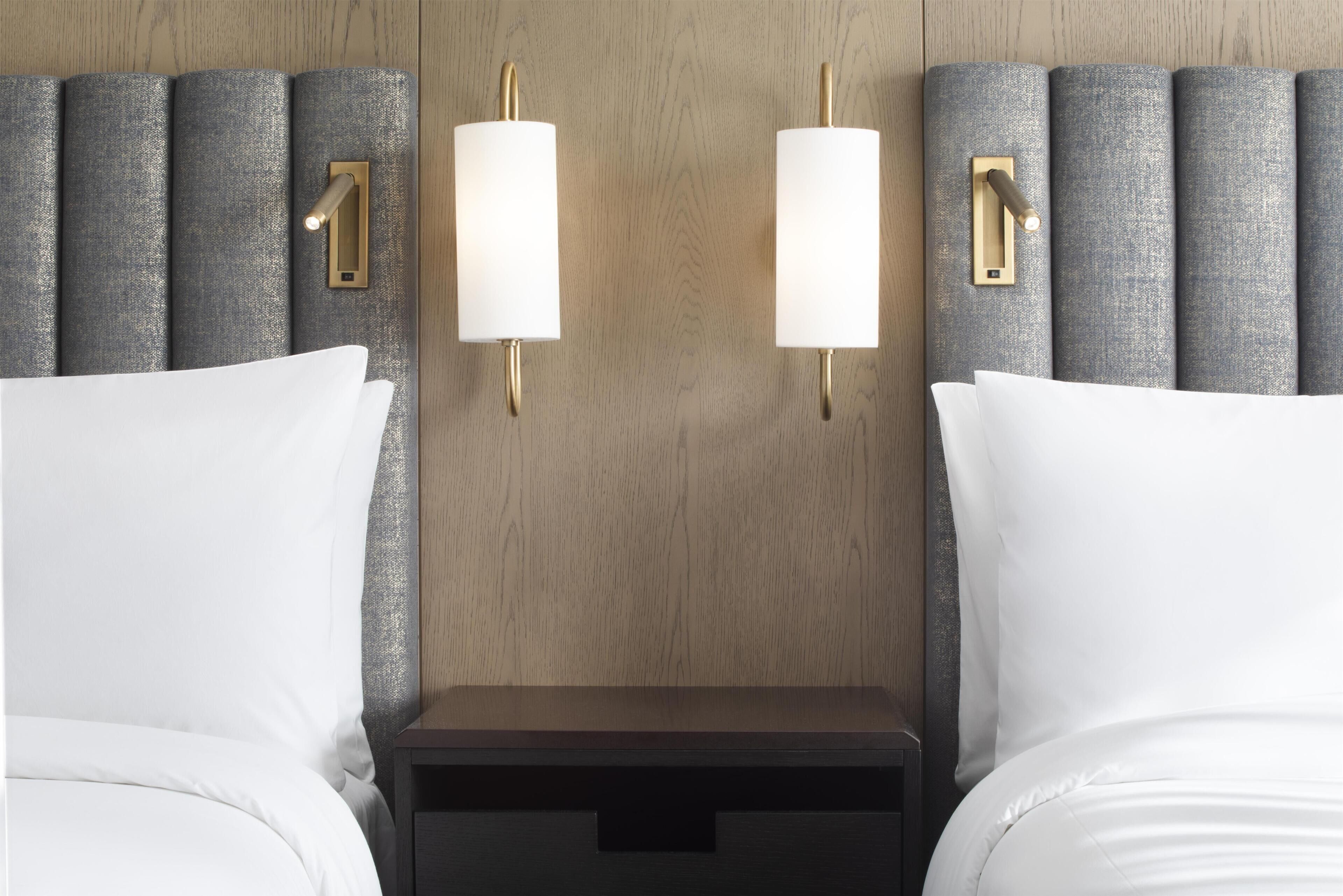 A hotel room with a wooden headboard, two bedside tables, and white bedding.