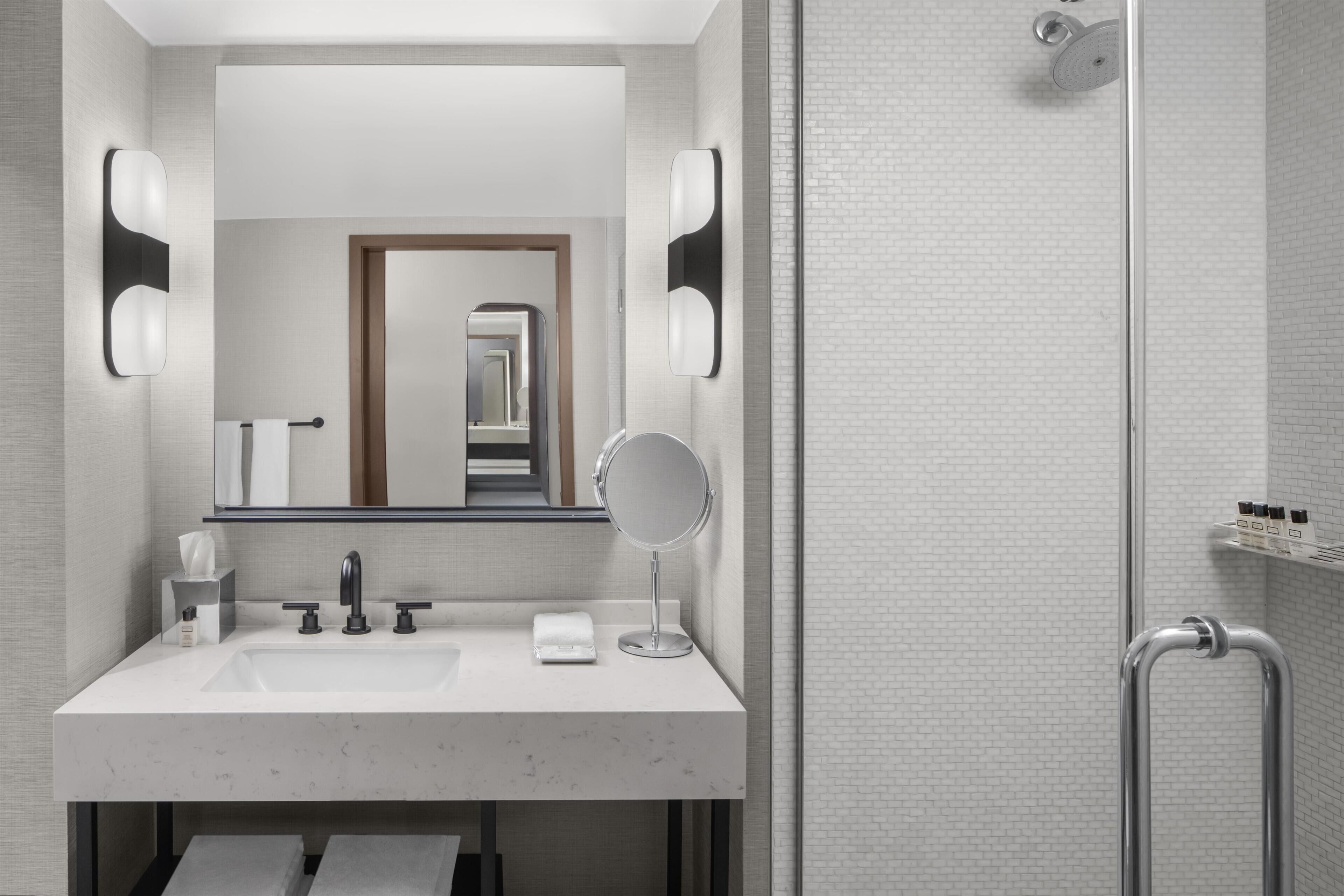Une salle de bain moderne avec un grand miroir, deux lavabos, un porte-serviettes et un espace douche.