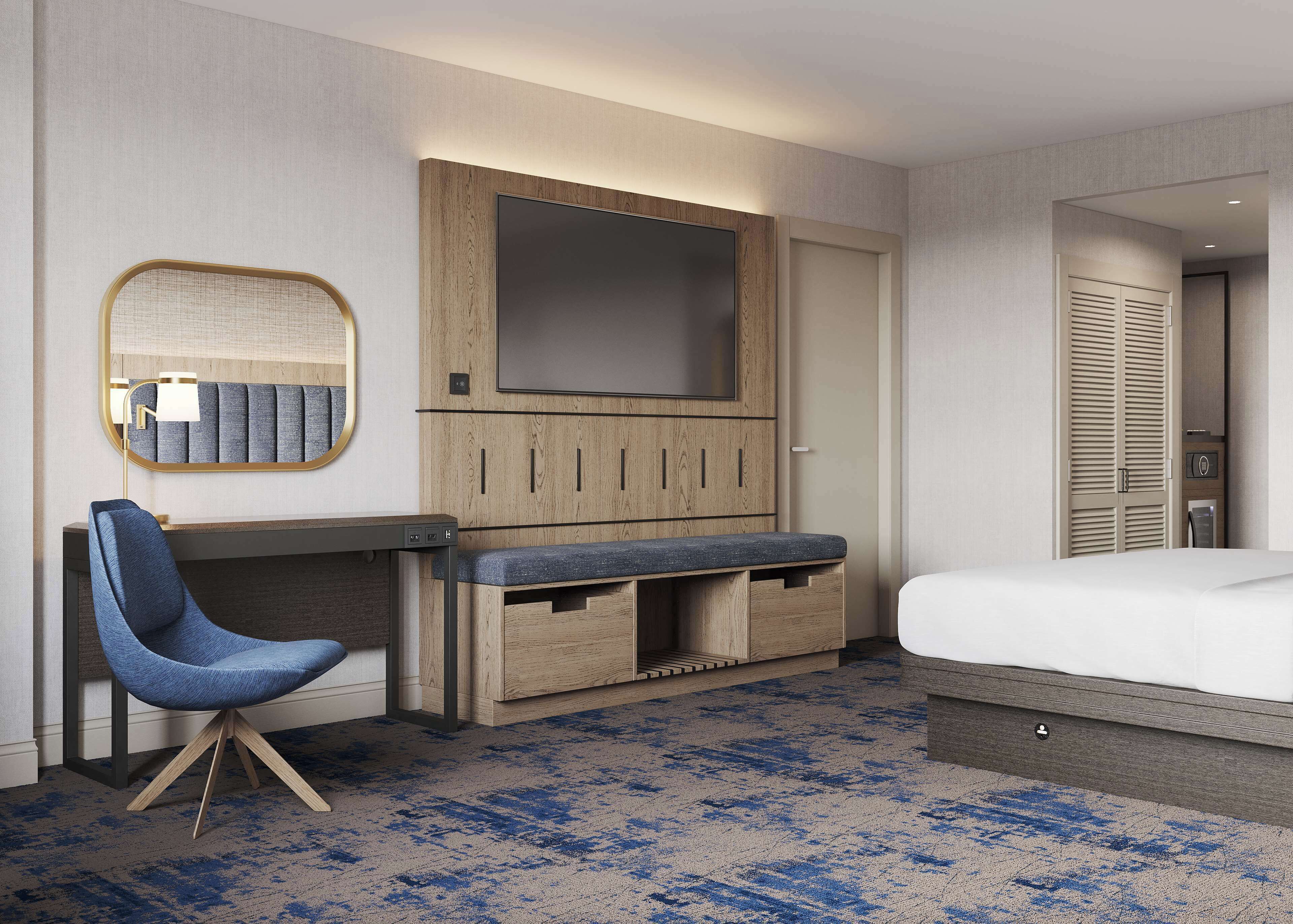 A hotel room with a bed, a desk with a chair, a TV, and a wardrobe.