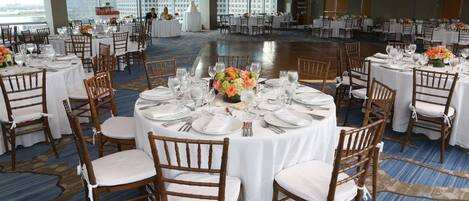 Un salón de banquetes con mesas redondas dispuestas para un evento formal, con manteles blancos, centros de mesa florales y sillas de madera.