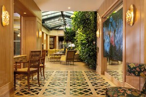 A hotel lobby with a high ceiling, a glass skylight, a green wall with plants, and a patterned floor. - Hotel Pas De Calais (Paris)