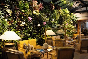 A room with a large green wall of plants, yellow sofas, and wooden tables with lamps. - Hotel Pas De Calais (Paris)