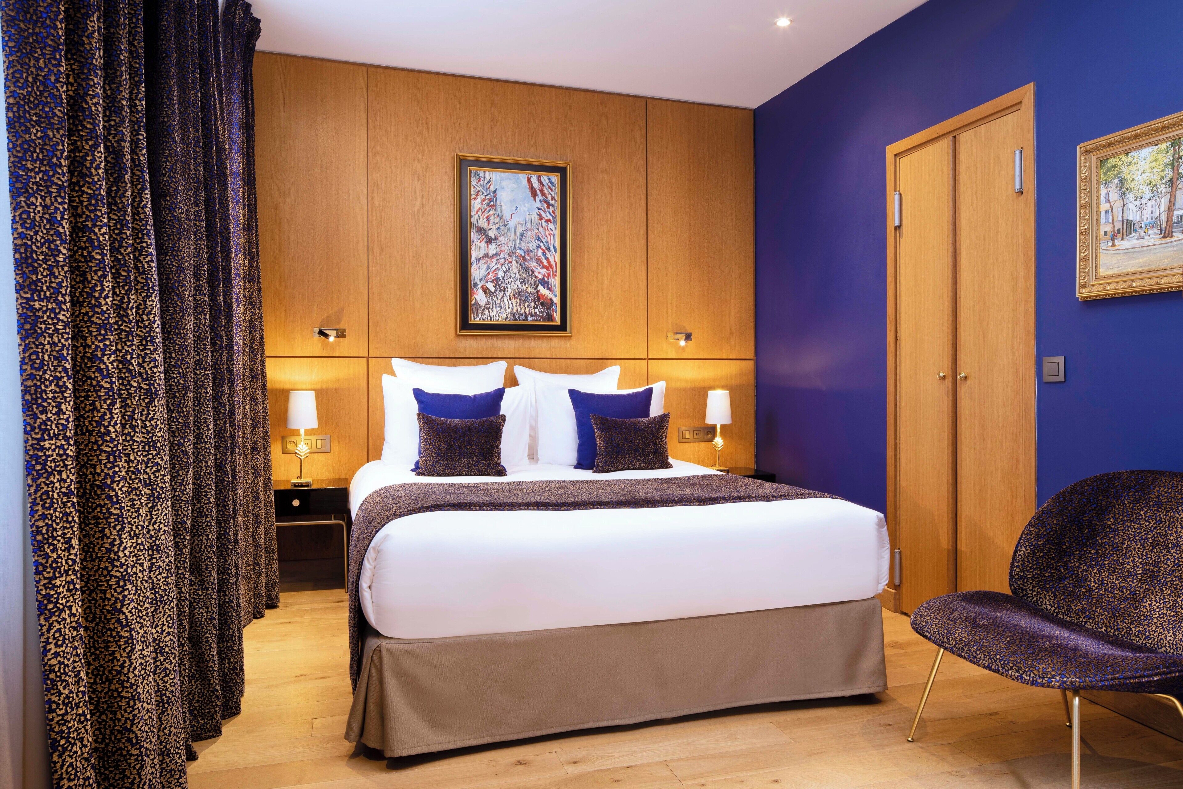 A hotel room with a large bed, two bedside tables with lamps, a wooden wardrobe, and a framed picture on the wall.