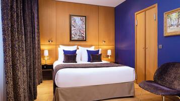 A hotel room with a large bed, two bedside tables with lamps, a wooden wardrobe, and a framed picture on the wall.