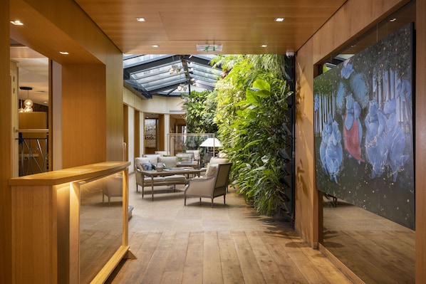 A spacious lobby with wooden flooring, a reception desk, seating area, and a large wall mural. - Hotel Pas De Calais (Paris)