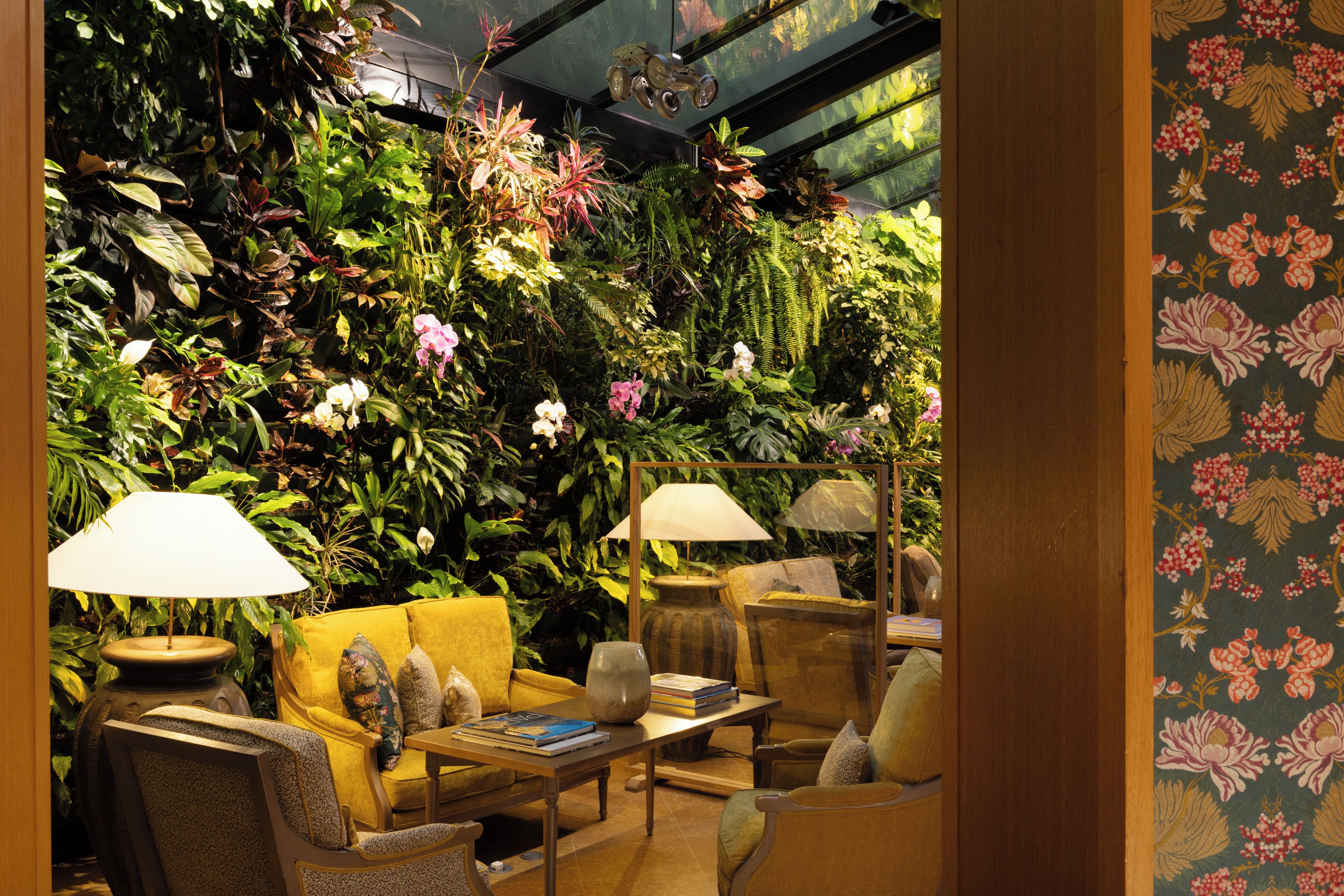 Una habitación con una pared verde cubierta de plantas, un sofá amarillo y dos lámparas.