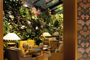 A room with a green wall covered in plants, a yellow sofa, and two lamps. - Hotel Pas De Calais (Paris)