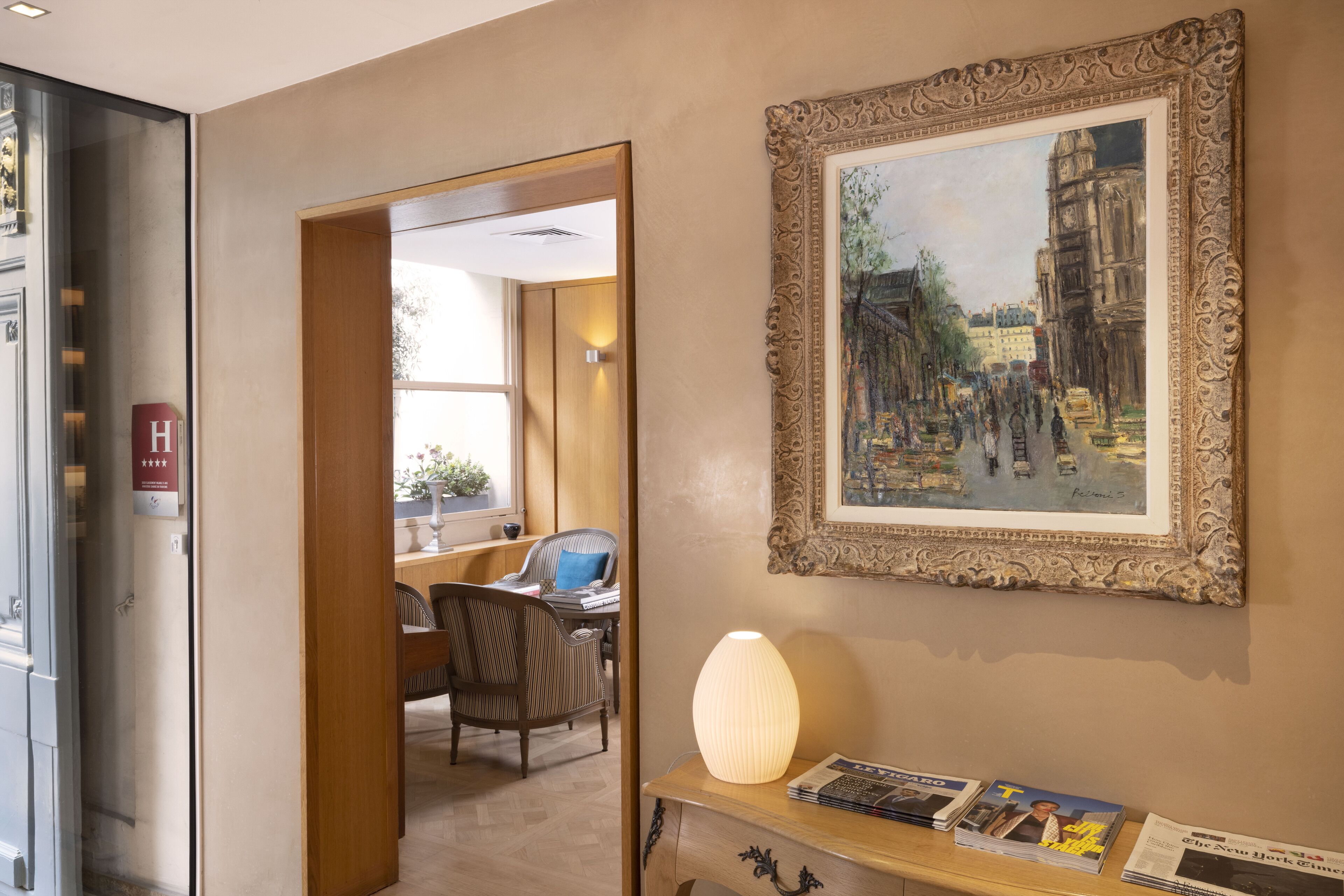 A hotel lobby with a framed painting, a desk with magazines, and a lamp.