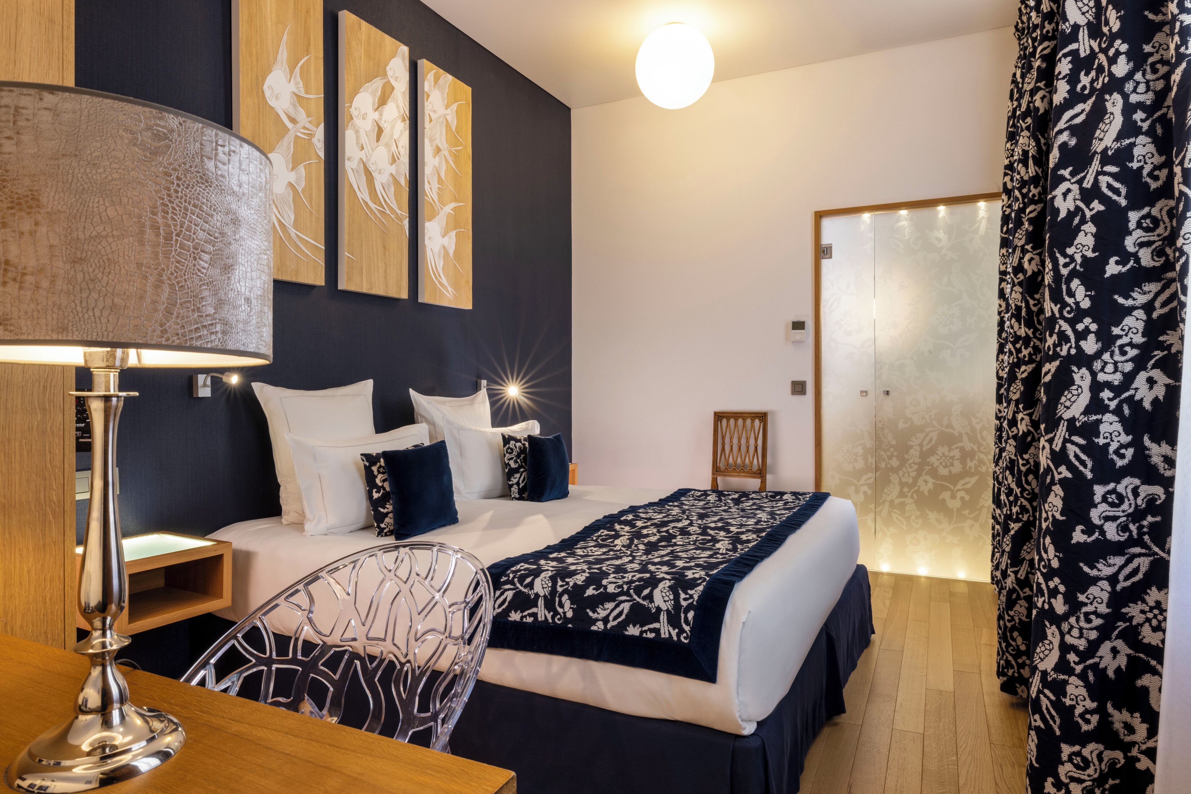 A hotel room with a bed, bedside table, lamp, chair, and artwork on the wall.