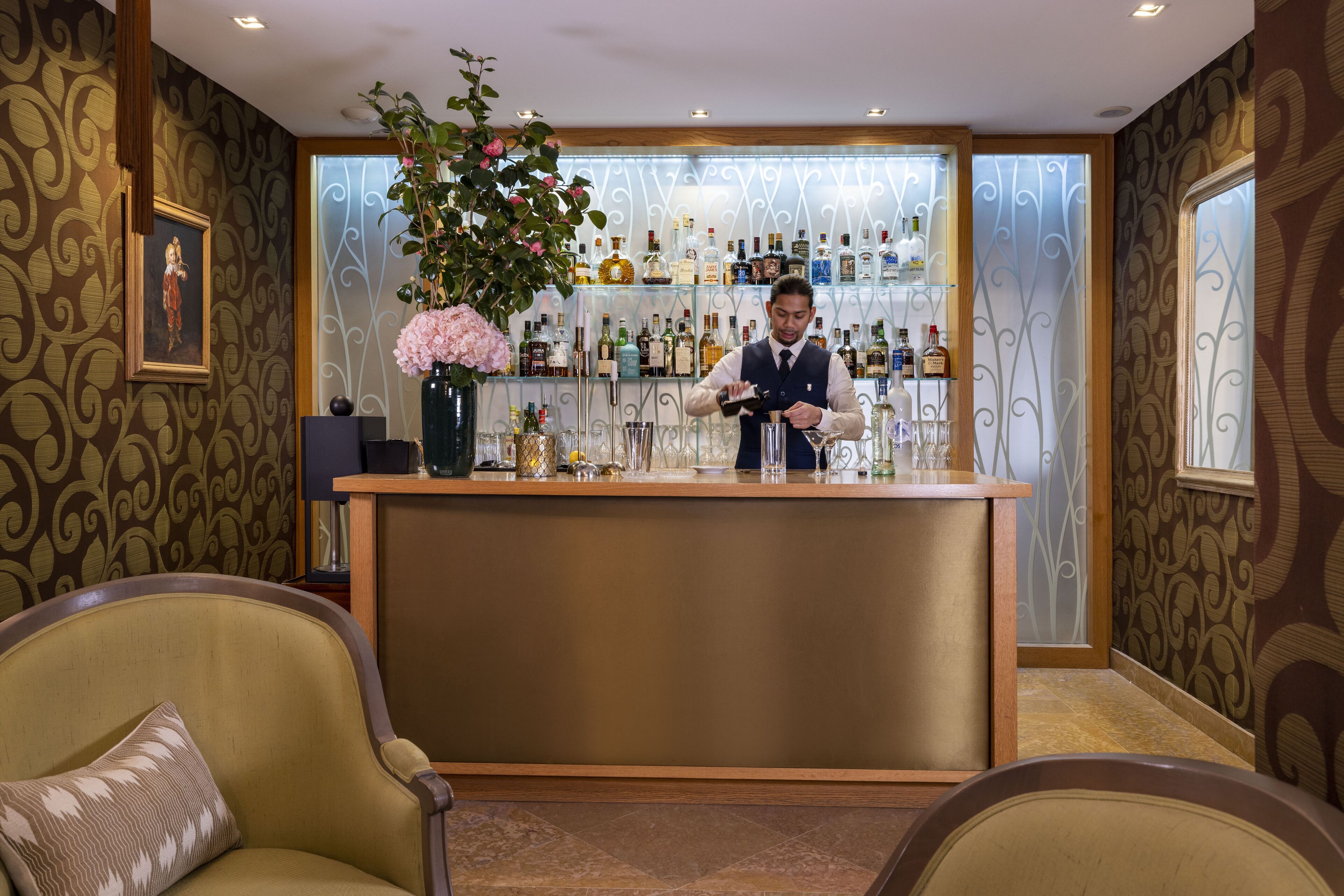 A bar area with a bartender, a large floral arrangement, and a shelf of liquor bottles.