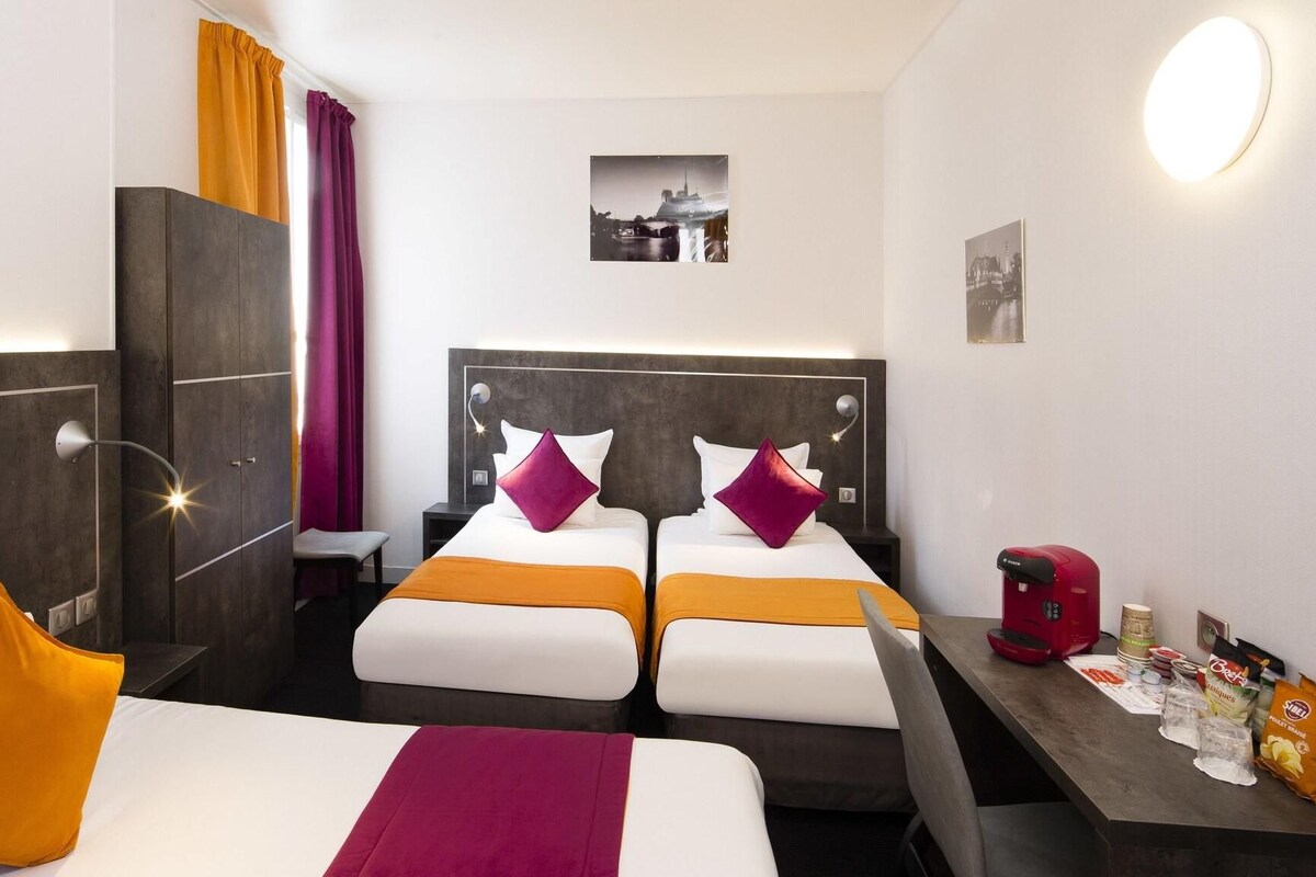 A hotel room with two beds, a desk with a coffee machine, and a minibar.