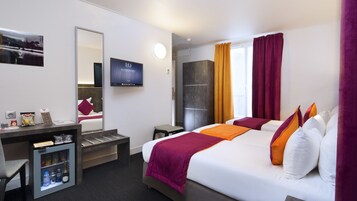 A hotel room with a bed, a desk with a computer, a TV, and a minibar.