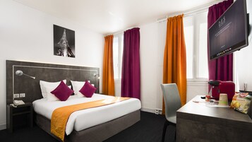 A hotel room with a bed, a desk, a chair, a television, and a window with curtains.