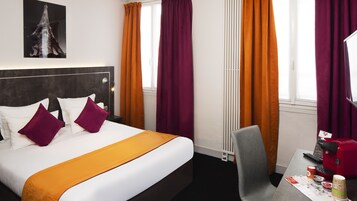 A hotel room with a bed, a desk with a red coffee maker, a chair, and a window with curtains.