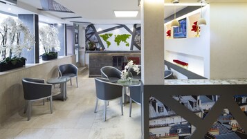 A modern hotel lobby with a reception desk, seating area with chairs and tables, decorative plants, and a view of the cityscape through large windows.