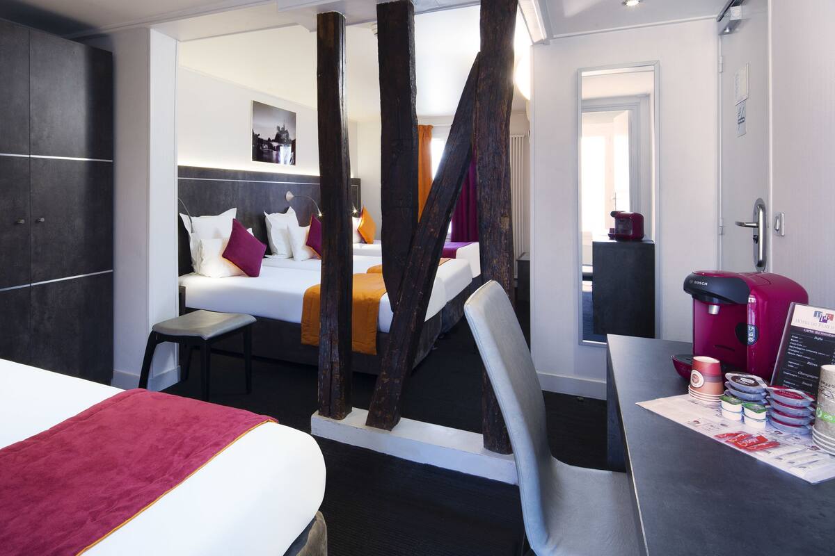 Una habitación de hotel moderna con una cama grande, un escritorio con cafetera y vista al pasillo.