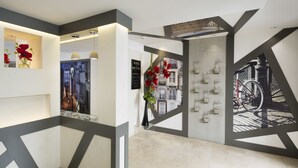 Un moderno vestíbulo de hotel con diseños geométricos en las paredes, una obra de arte con una vista urbana enmarcada y un jarrón con flores rojas.