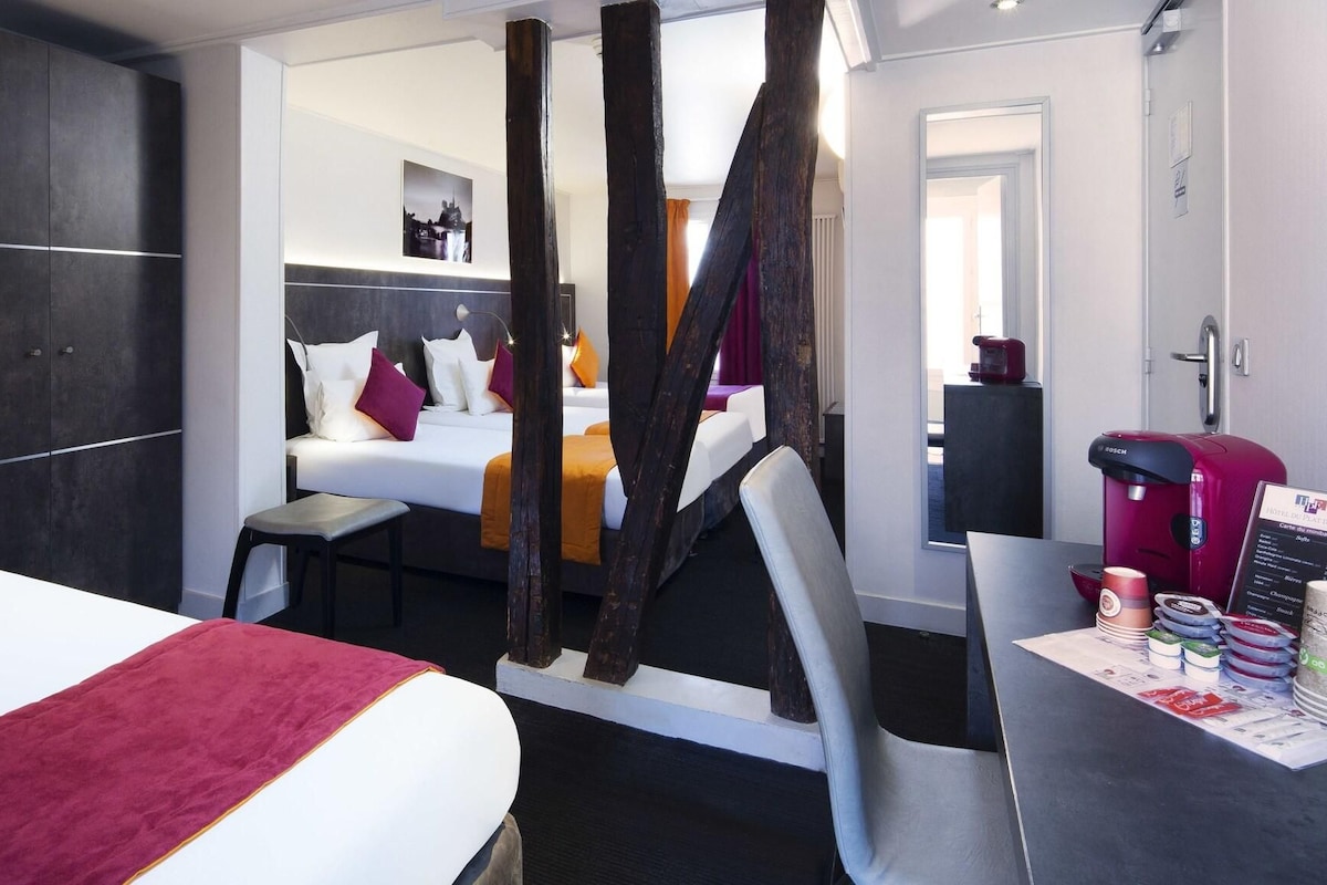 A hotel room with a bed, a desk with a coffee maker, and a view of the hallway.