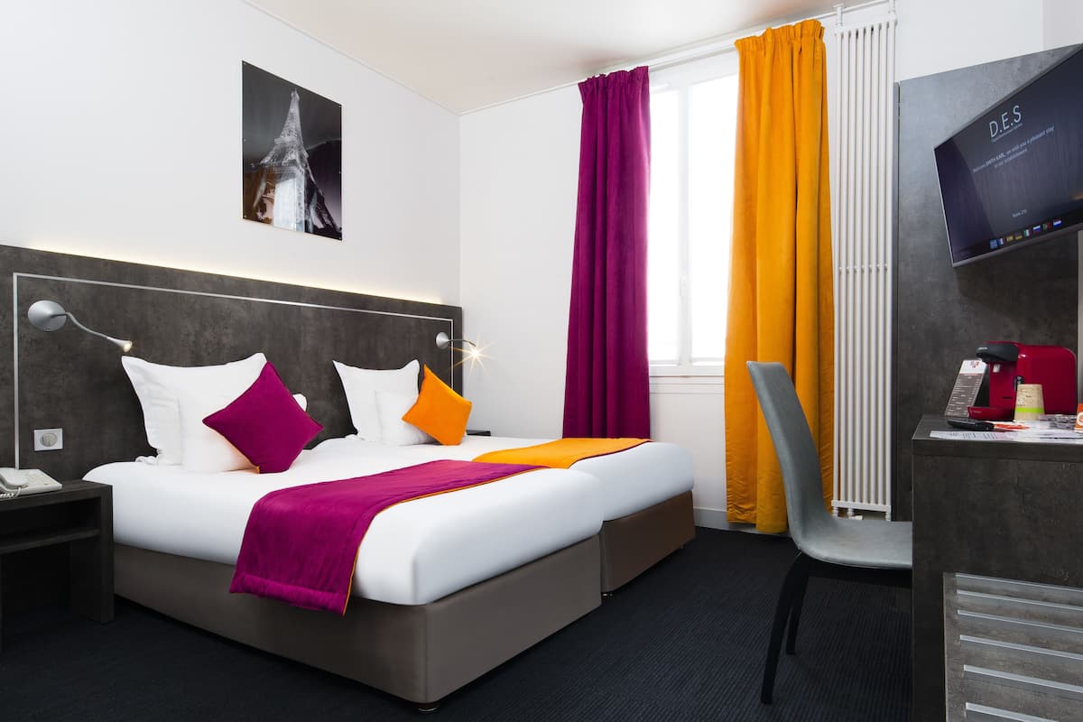 Habitación de hotel con cama, escritorio con computadora, silla, televisión y ventana con cortinas.