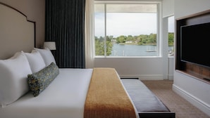 A hotel room with a large bed, a TV, and a window with a view of a lake and buildings. - The Tides Inn (Irvington)